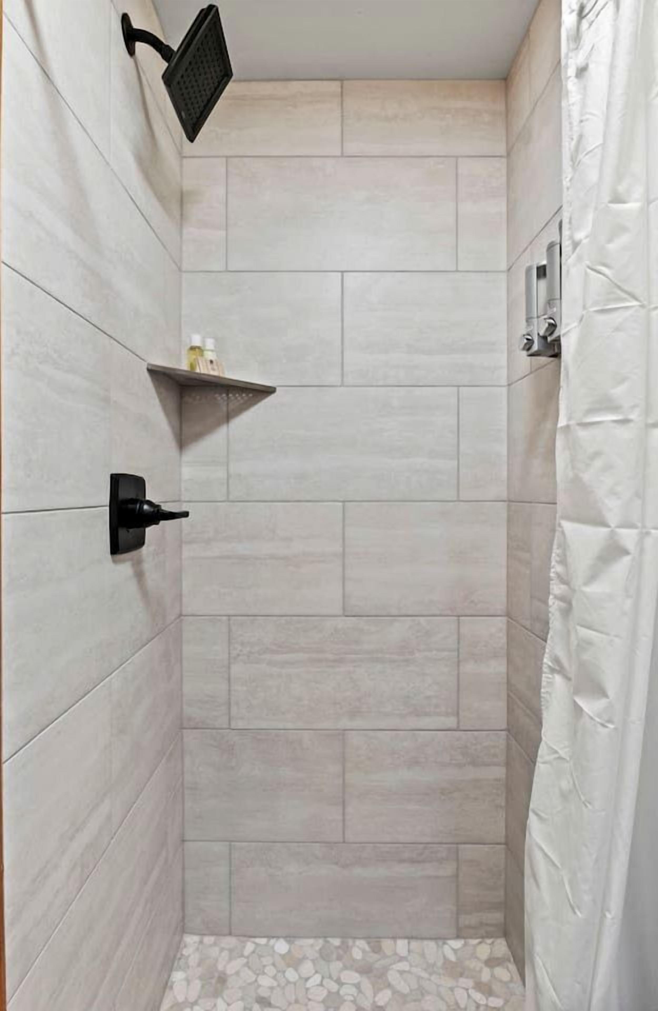 A shower area with tiled walls, a showerhead, a shelf with toiletries, and a shower curtain.