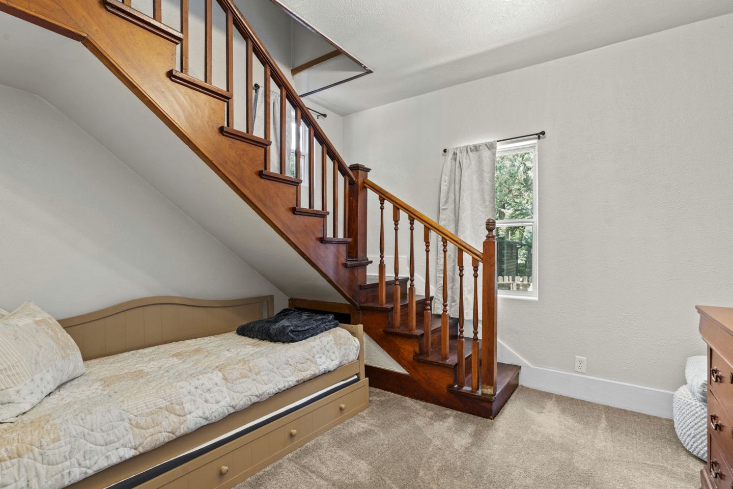 Un dormitorio con una cama individual, una escalera de madera, una ventana con cortinas y un aparador.
