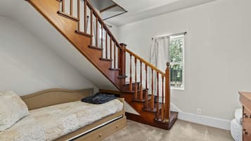 Un dormitorio con una cama individual, una escalera de madera, una ventana con cortinas y un aparador.