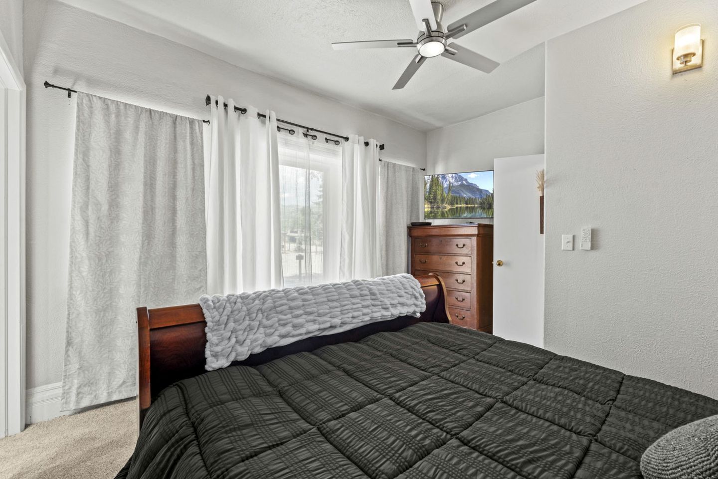 Un dormitorio con cama, ventilador de techo, cómoda y ventana con cortinas.
