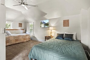 Ein Schlafzimmer mit einem Bett, einem Einzelbett, einem Nachttisch, einer Lampe, einem Deckenventilator und einem Fenster.