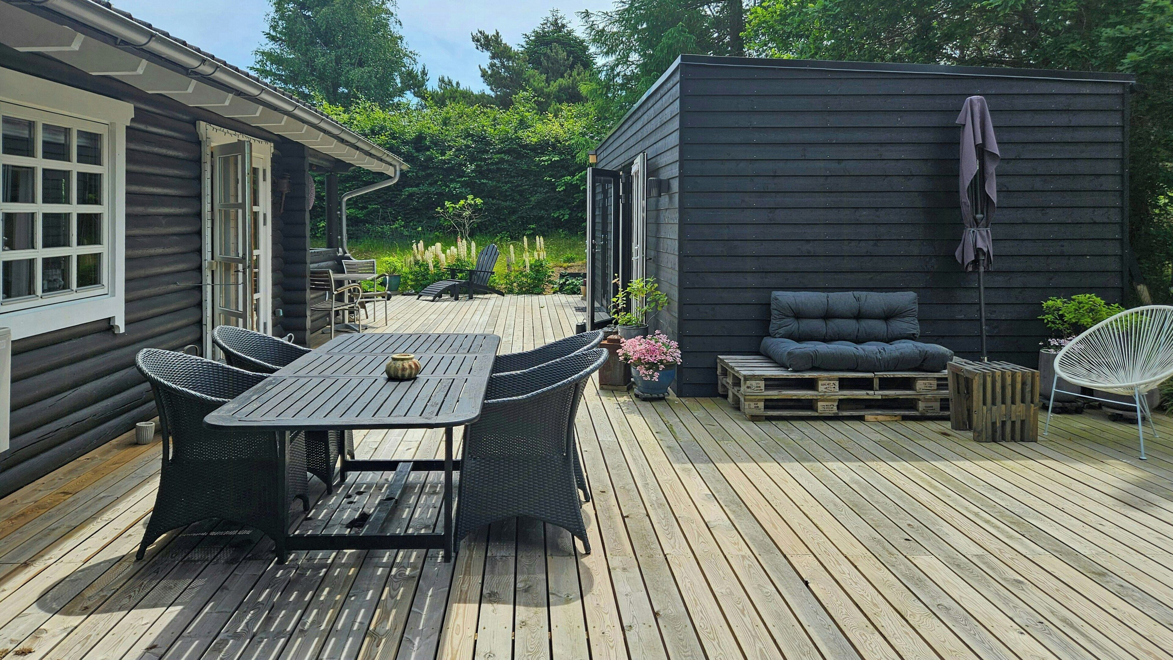 A wooden deck with a table and chairs, a sofa, and a small garden area.