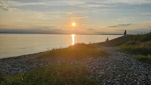 Een zonsondergang boven kalm water, met een rotsachtige kustlijn en iemand die op de rand zit.