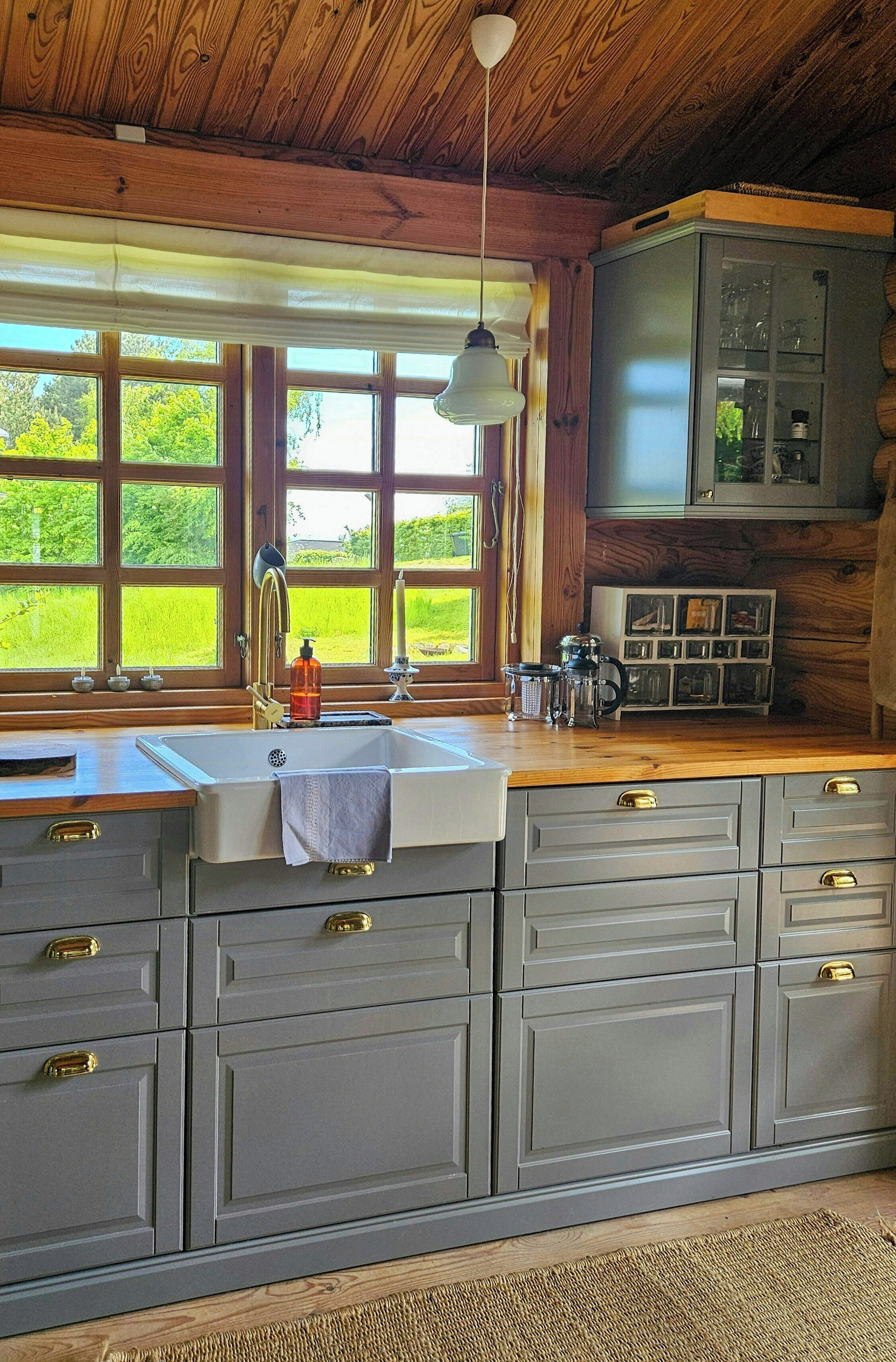 Eine Küche mit großem Fenster, Holzbalkendecke und grauen Schränken.