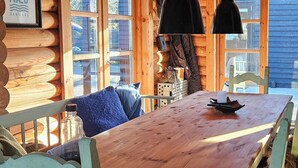 Een rustiek houten interieur met een lange eettafel, stoelen met bont plaids en een opgehangen dieren schedel.