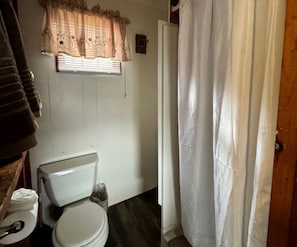 Ein kleines Badezimmer mit Toilette, einem Fenster mit blumigem Vorhang und einer Duschvorhang.