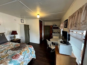 Ein kompaktes Zimmer mit einem Bett, einem Schreibtisch mit Computer, einem Stuhl und einer Küchenzeile.