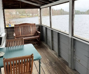 Ein überdachter Außenbereich mit Holzmöbeln, einem Tisch und Blick auf einen See.