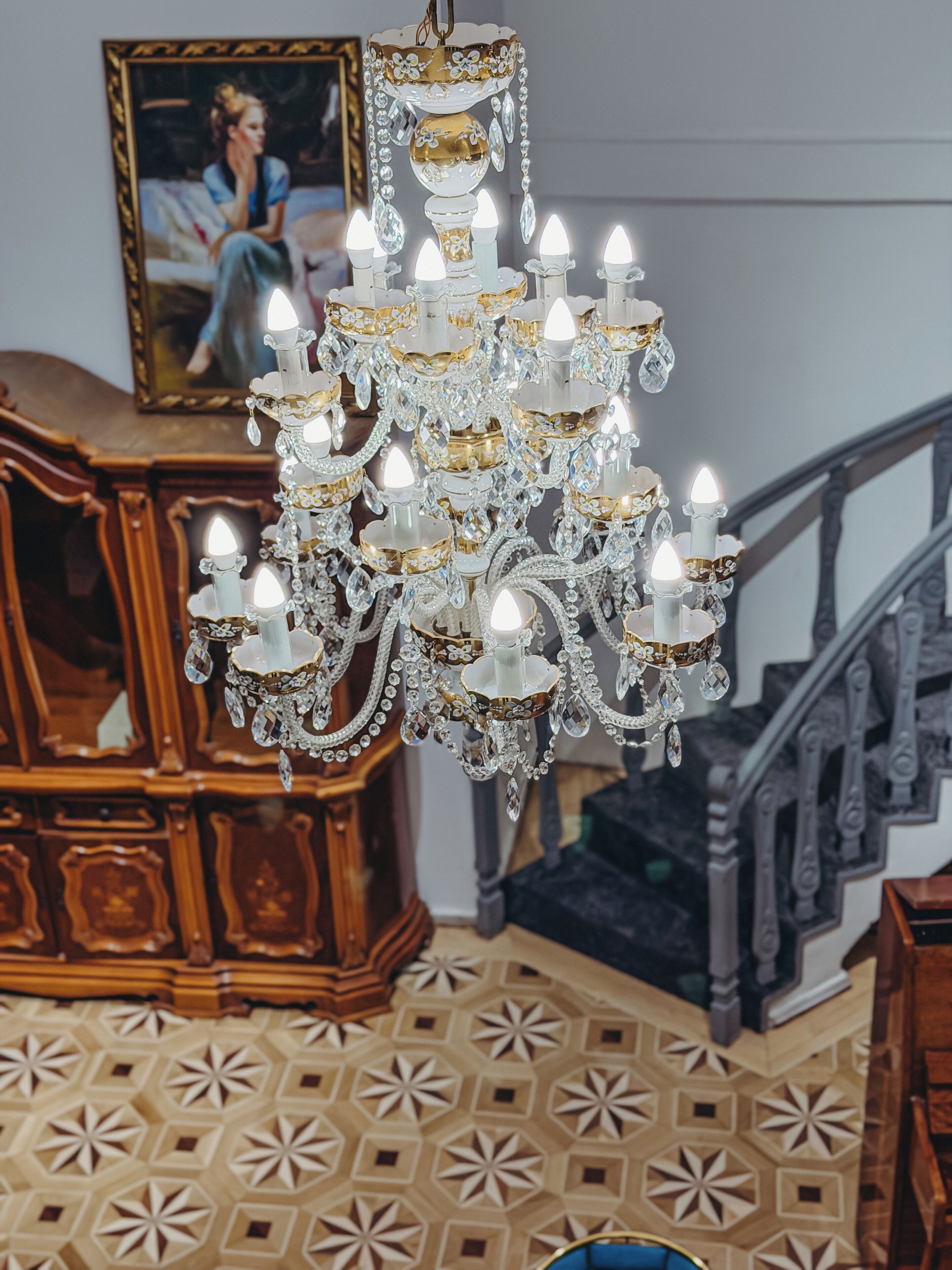 A chandelier with multiple candles, a wooden cabinet, and a staircase.