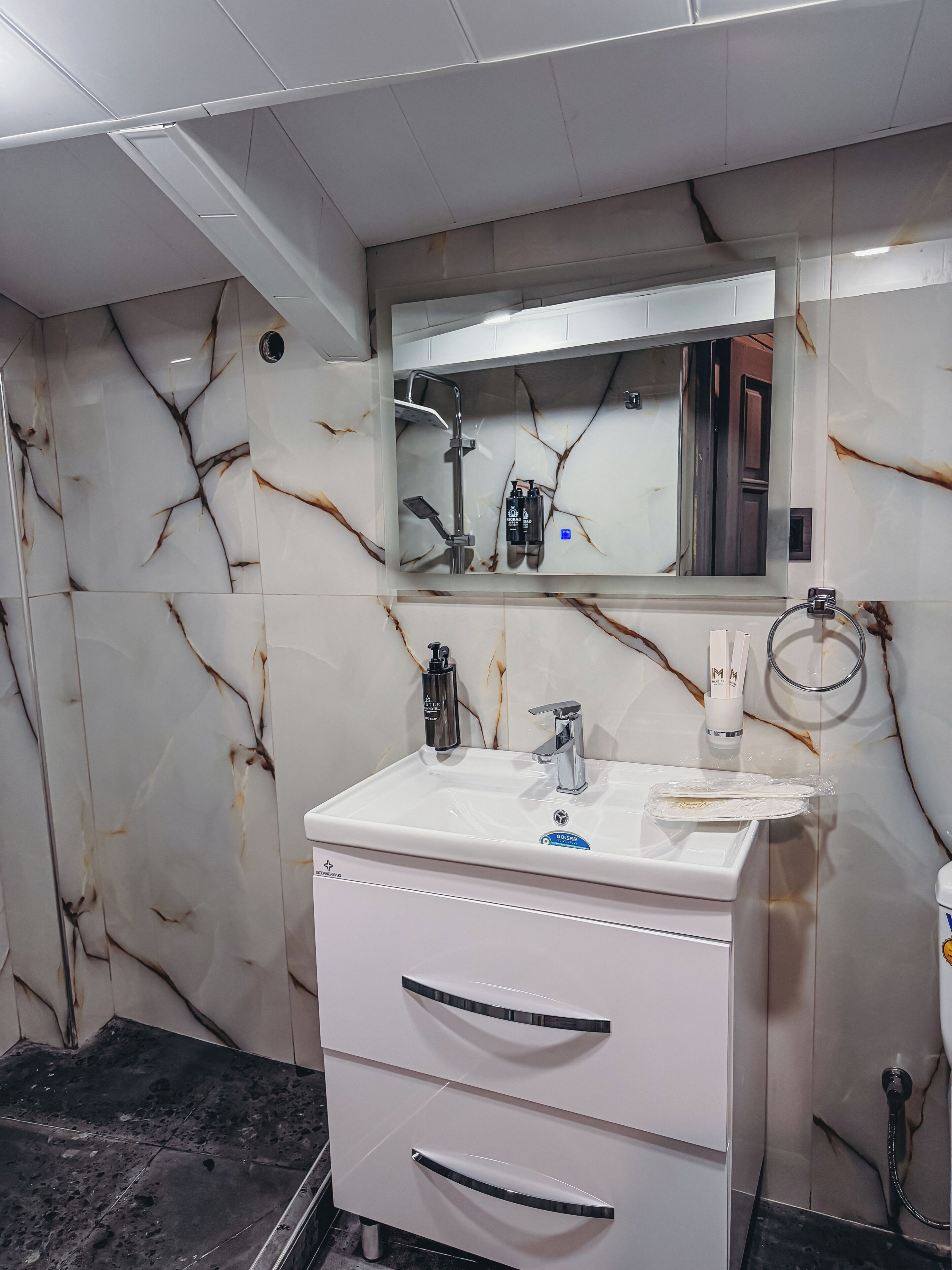 A bathroom with a white vanity, a mirror, a shower, and marble walls.