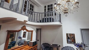 A spacious living area with a high ceiling, a chandelier, a wooden cabinet, and a dining table. - Pushkin Hotel Yerevan (Yerevan)