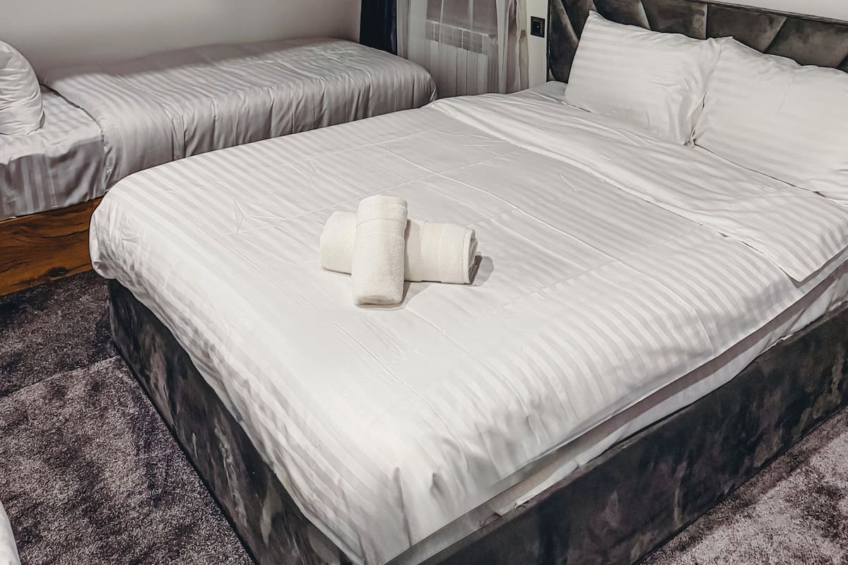 Hotellihuone, jossa on kaksi sänkyä, tumma pääty, ikkuna verhoilla ja ilmastointilaite.
