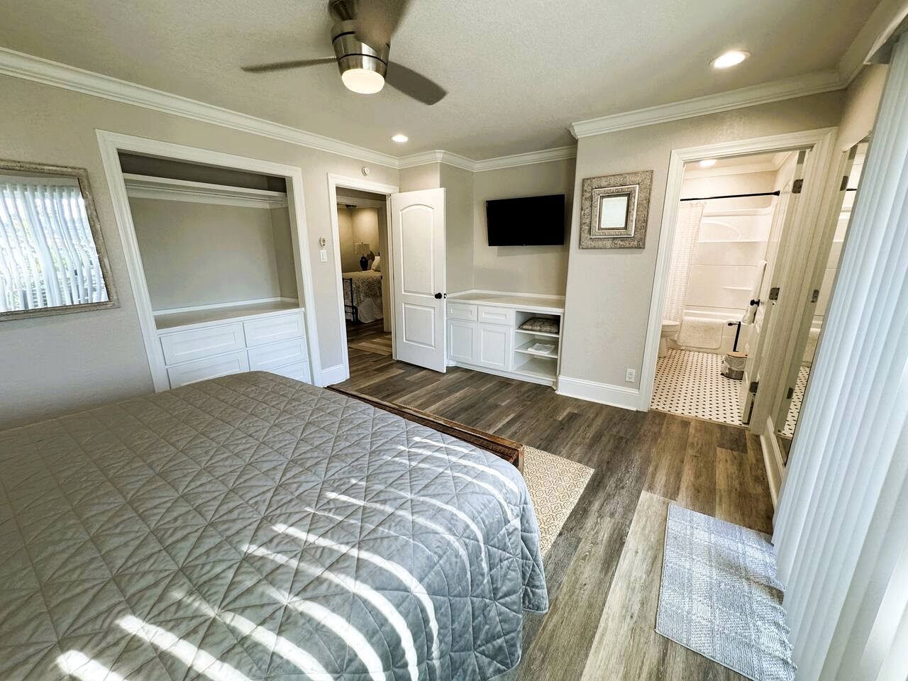 A bedroom with a bed, a ceiling fan, a TV, a walk-in closet, and a bathroom.