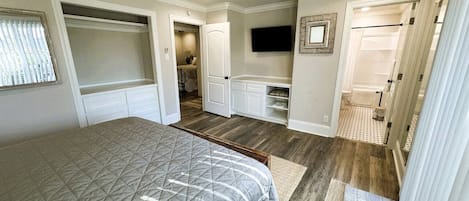 A bedroom with a bed, a ceiling fan, a TV, a walk-in closet, and a bathroom.