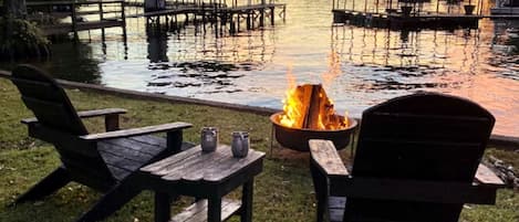 A lakeside setting with wooden chairs and a fire pit.