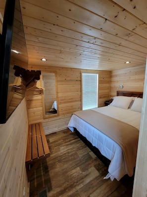 A wooden cabin room with a bed, a bench, a window, and a mirror. - Peaceful Desert Escape in a Stylish New Tiny Home in Williams, Arizona (Williams)