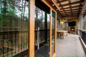 An outdoor deck with a wooden railing, a stone fireplace, and a bench. - Luxury Escape Perfect for Families with Private Hot Tub, Infrared Sauna & Vintage Jukebox in  Broken Bow, Oklahoma (Broken Bow)