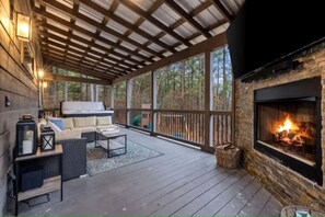 A covered deck with a fireplace, outdoor seating, and a view of the surrounding forest. - Luxury Escape Perfect for Families with Private Hot Tub, Infrared Sauna & Vintage Jukebox in  Broken Bow, Oklahoma (Broken Bow)