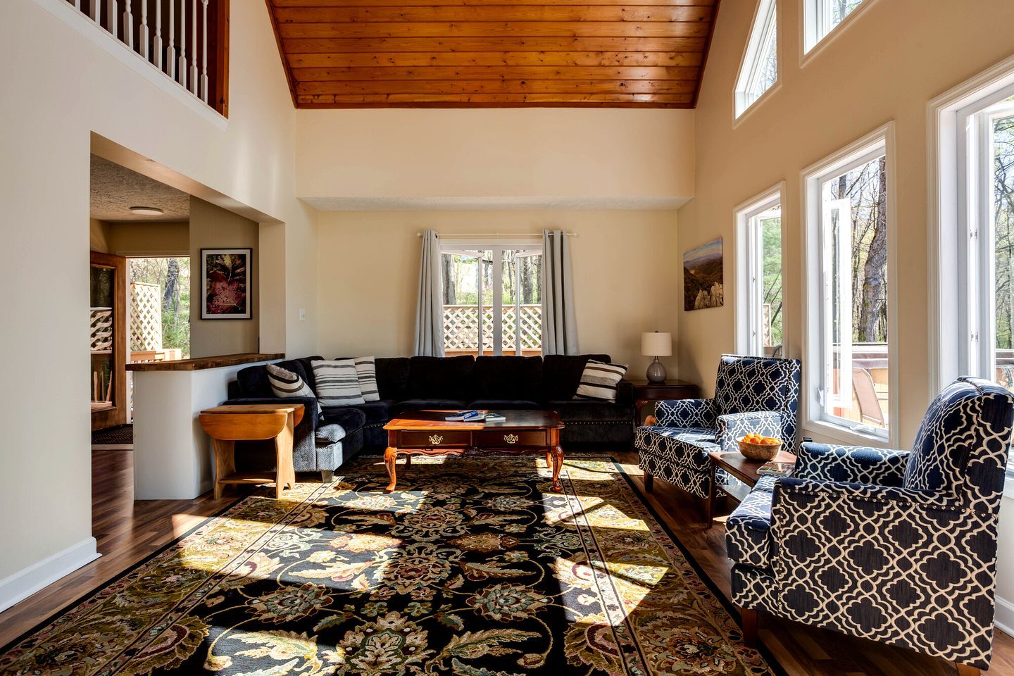 A spacious living room with a high ceiling, a large window, and a patterned rug.