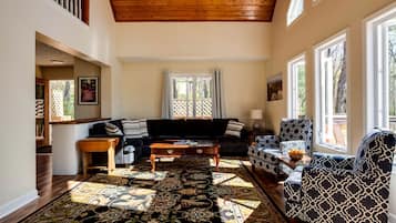 A spacious living room with a high ceiling, a large window, and a patterned rug.