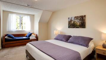 A bedroom with a large bed, a smaller bed, a window with curtains, a painting on the wall, and a bedside table with a lamp.