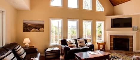 A spacious living room with a fireplace, leather sofas, and large windows.