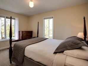 A bedroom with a four-poster bed, a dresser, and two windows.