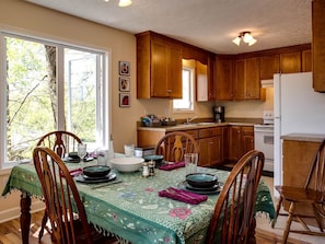 Un comedor con sillas de madera, una mesa preparada para cuatro personas y una cocina al fondo.