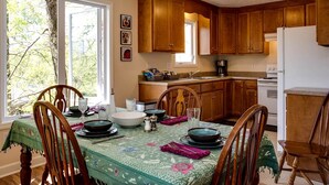 A dining area with wooden chairs, a table set for four, and a kitchen in the background. - Family Time in Love, Virginia: Mountain Cabin Getaway (Love)