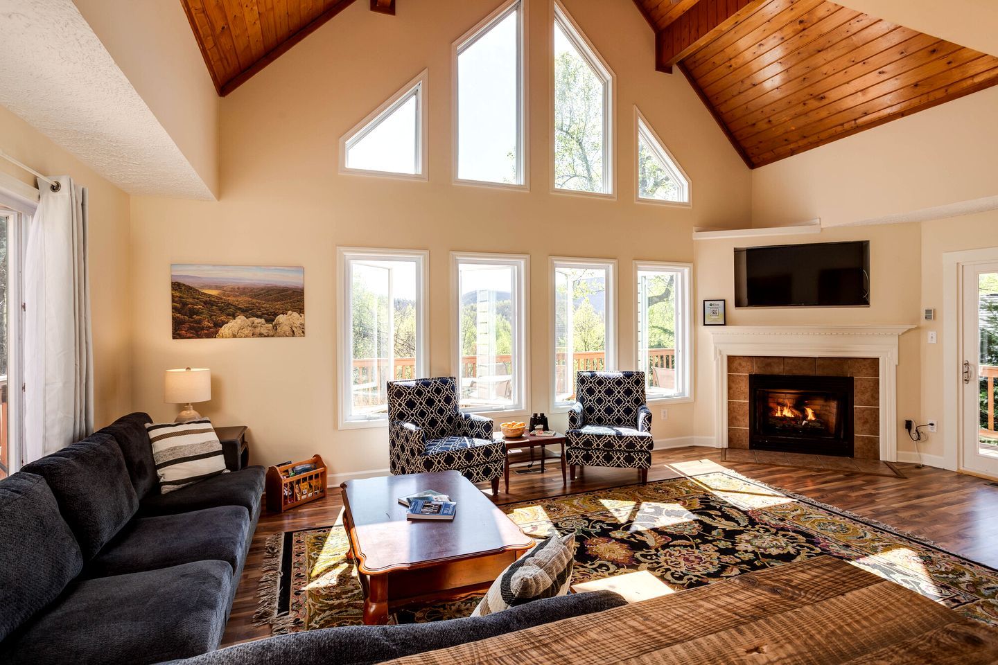 A spacious living room with a fireplace, large windows, and a high ceiling.