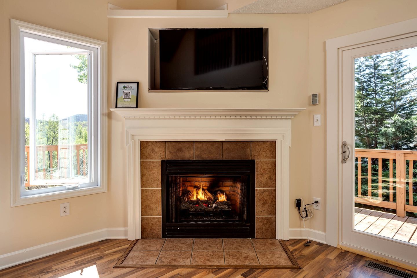 Una habitación con chimenea, televisor montado encima y vista al exterior a través de una puerta.
