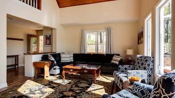 Uma sala de estar ampla, com um sofá escuro, poltronas estampadas, uma mesa de centro de madeira e um tapete grande.