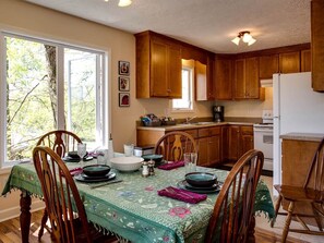 A dining area with wooden chairs, a table set for four, and a kitchen in the background.