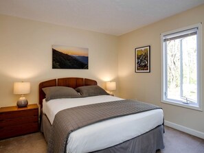 A bedroom with a bed, two bedside tables, a window, and two wall-mounted pictures.
