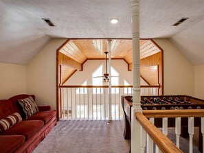 A loft bedroom with a red sofa, a foosball table, and a wooden ceiling.