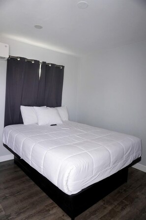 A single bed with a white mattress and dark headboard, a small bedside table, and a wall-mounted air conditioning unit. - Quiet Escape Studio Perfect for Exploring Natural Wonders in Williams, Arizona (Williams)