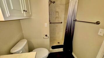 A small bathroom with a toilet, a shower with a curtain, and a towel rack.