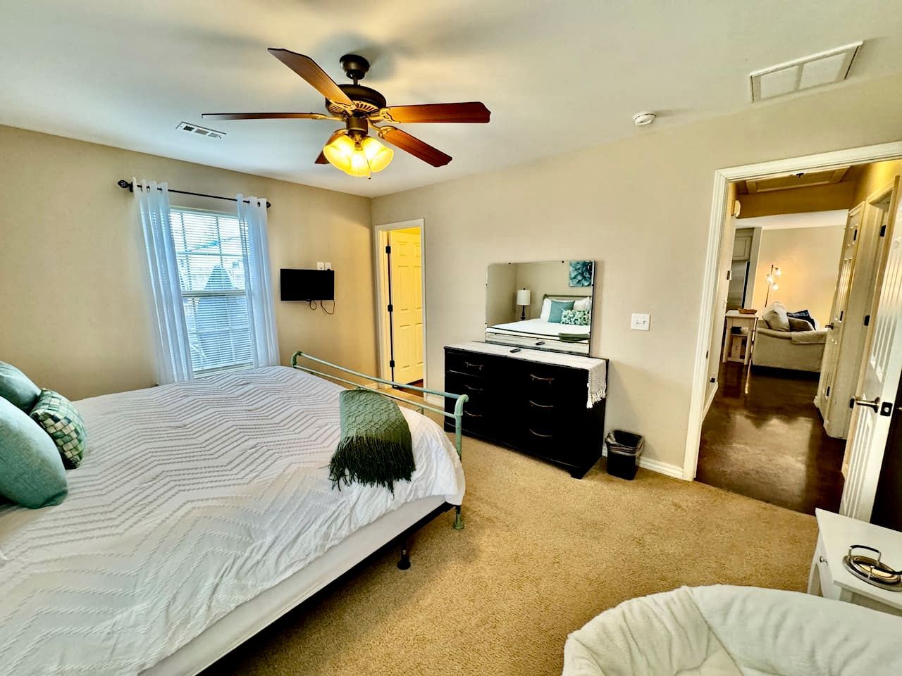 A bedroom with a bed, a dresser, a ceiling fan, and a door leading to another room.