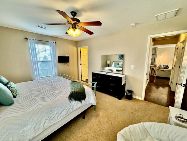 A bedroom with a bed, a dresser, a ceiling fan, and a door leading to another room.