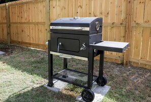 Un barbecue portable sur roulettes, dotĂ© dâune table dâappoint et dâun tiroir de rangement, placĂ© devant une clĂŽture en bois.