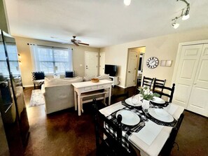 A dining area with a table set for four, a sofa, a television, and a ceiling fan.