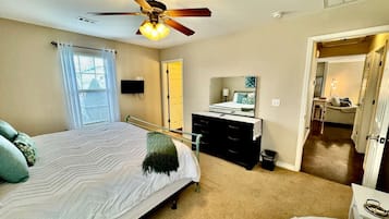 A bedroom with a bed, a dresser, a ceiling fan, and a door leading to another room.