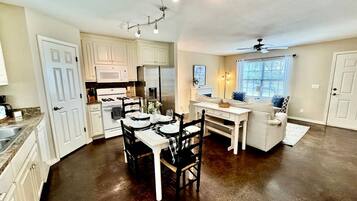 A kitchen with white cabinets, a dining table set for four, and a ceiling fan.