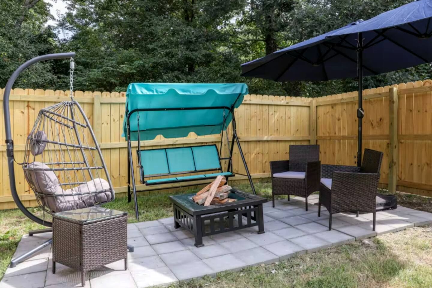 A patio with a swing chair, a table with wood, wicker chairs, and an umbrella.