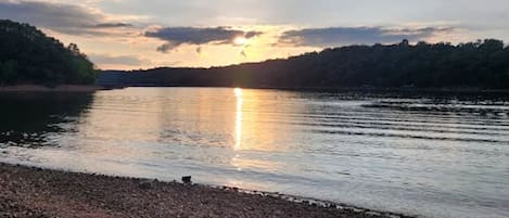 Un lago tranquilo con una orilla rocosa y árboles al fondo.