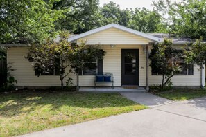 A single-story house with a front porch, a bench, and a small tree.