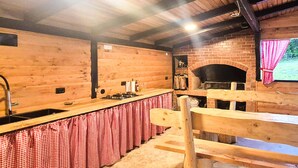 Une cuisine rustique aux murs en bois, avec un four en briques et une nappe à carreaux.