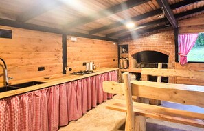 Eine rustikale Küche mit Holzwänden, einem Backofen aus Ziegeln und einer karierten Tischdecke.