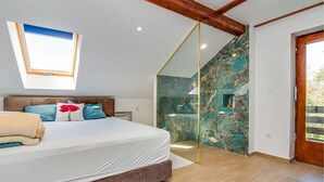 Une chambre avec un lit, une lucarne, une douche aux murs en marbre et un plafond en bois.