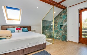 Ein Schlafzimmer mit Bett, einem Oberlicht, einer Dusche mit Marmorwänden und einer Holzbalkendecke.